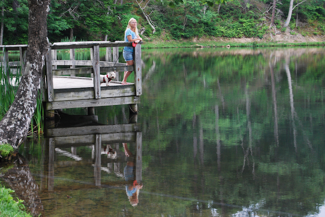 Photo of Carolyn and Sparky at the lake with reflections of green trees in the still water